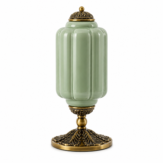 A decorative ceramic table lamp with a pale sage green ribbed body and ornate antique gold metal base and lid, shown on a plain white background.