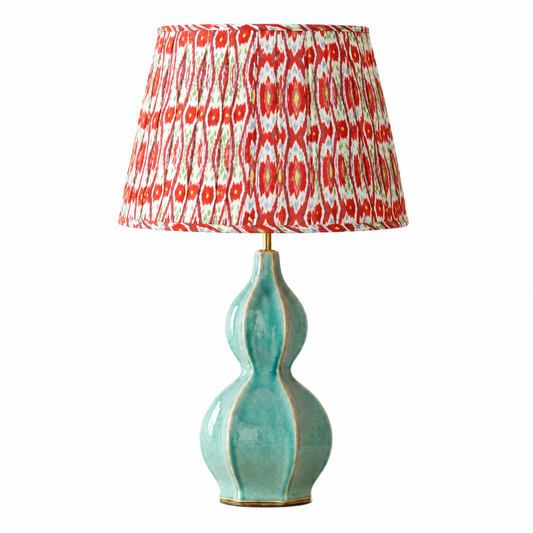 A table lamp with a glossy turquoise-green ceramic gourd-shaped base and a patterned drum shade featuring red, white, and orange ikat-style motifs, shown on a plain white background.